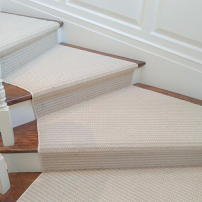 A close-up view of carpeted stairs with wooden risers and white wainscoting on the wall.